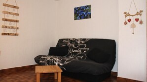 Un salón con un sofá estampado, una pequeña mesa de madera y adornos de pared, incluyendo un cuadro y dos adornos colgantes.
