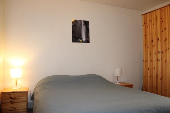 A bedroom with a bed, two bedside tables, a wooden wardrobe, and a wall-mounted picture.
