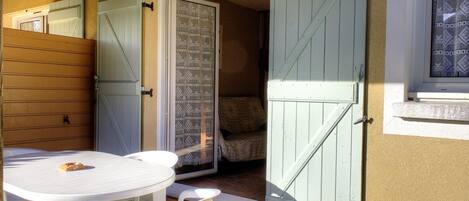 A patio with a round table and chairs, a wooden door, and a patterned curtain.