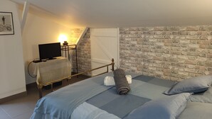 Un dormitorio con cama, televisión, escritorio y pared de ladrillo.