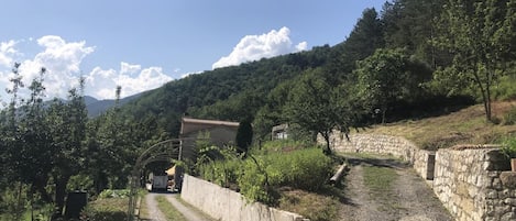 A rural road with a stone wall on one side and a building with a tiled roof in the distance.