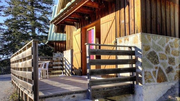 A wooden cabin with a stone foundation, a wooden porch, and a pink door.