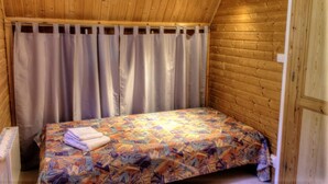 A small, cozy room with wooden walls and a sloped ceiling. It features a single bed with a colorful bedspread and a neatly folded towel.
