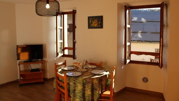 A dining area with a table set for four, a television on a stand, and a large window with an open shutter.