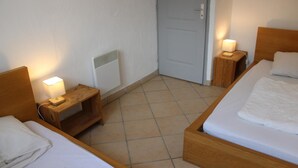 Une chambre d’hôtel avec deux lits en bois, une petite table de chevet en bois avec une lampe, un radiateur et une porte.
