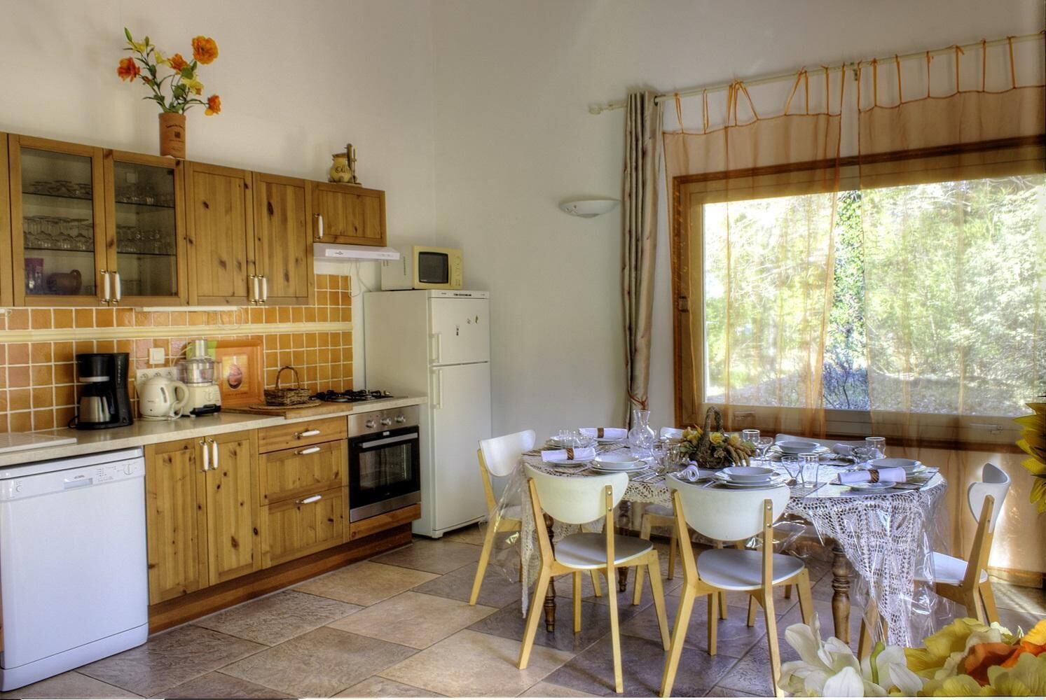 A kitchen with wooden cabinets, a refrigerator, a microwave, and a dining table set for four.