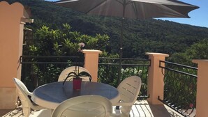 A balcony with a round table, white chairs, a potted plant, and a large umbrella.