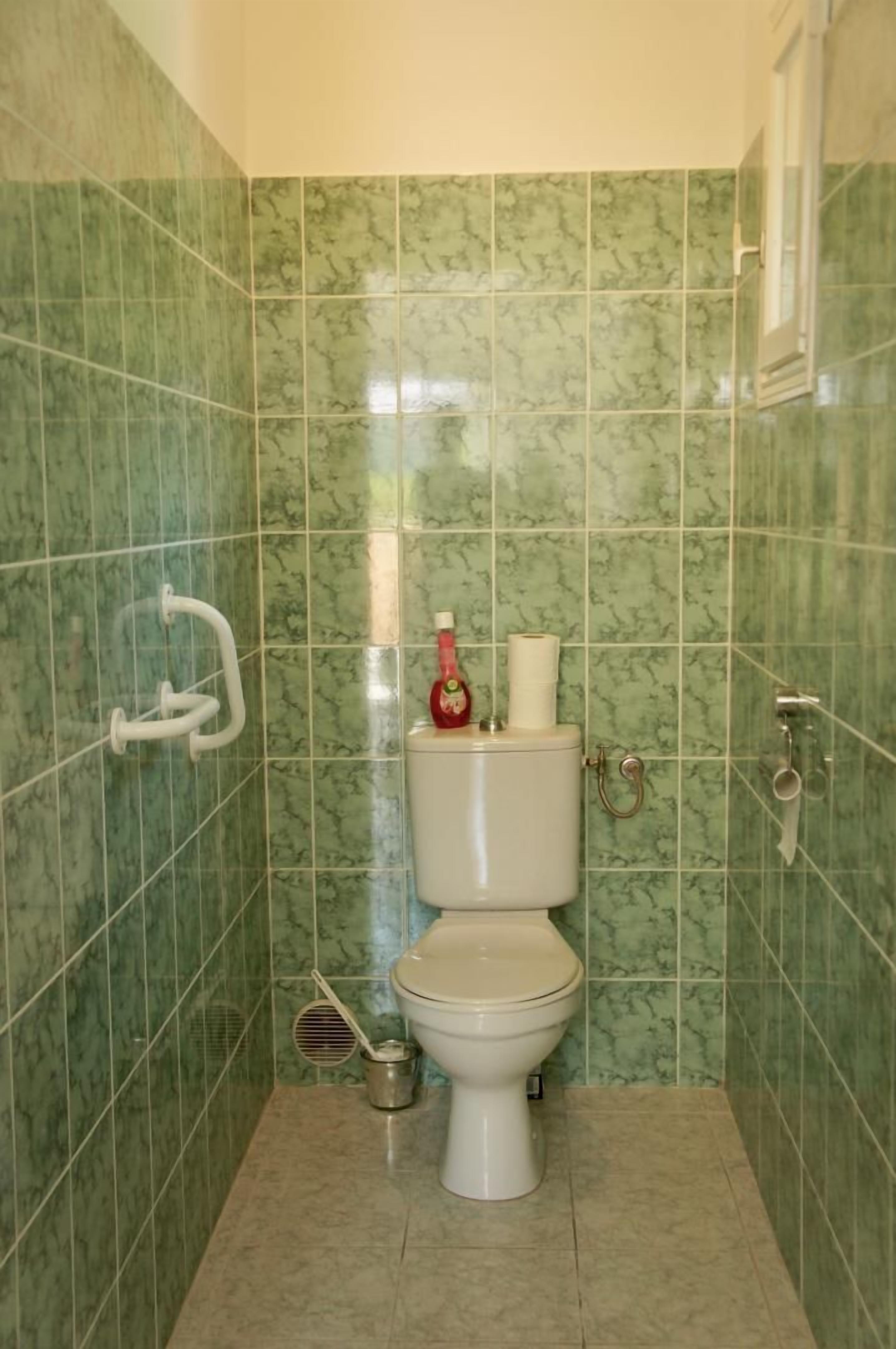 A bathroom with green marble tiles, a toilet, a bidet, and a handrail.