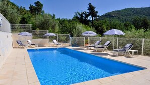 A rectangular swimming pool with clear blue water, surrounded by tiled flooring. There are lounge chairs and striped umbrellas around the pool.