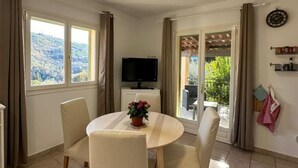 A dining area with a round table, four chairs, a potted plant, and a TV on a stand.