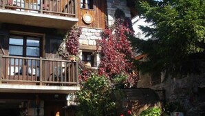 Un chalet de madera de dos pisos con balcones, paredes de piedra y una escalera de piedra que lleva a la entrada.