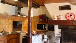 A kitchen with a stone wall, wooden cabinets, a stove, a microwave, and a fireplace.