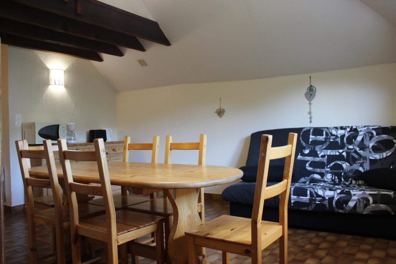 A dining area with a round wooden table and six chairs, a black and white patterned sofa, and a ceiling light fixture.