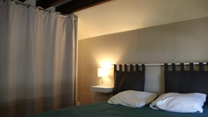 Une chambre à coucher avec un lit, une table de chevet, une lampe et un rideau.
