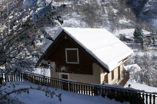 A wooden cabin with a snow-covered roof, surrounded by a wooden fence and snow-covered trees.