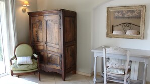 A room with a wooden cabinet, a green armchair, and a white table with a chair. - Cueille la Nuit - TOURRETTES-SUR-LOUP (TOURRETTES-SUR-LOUP)