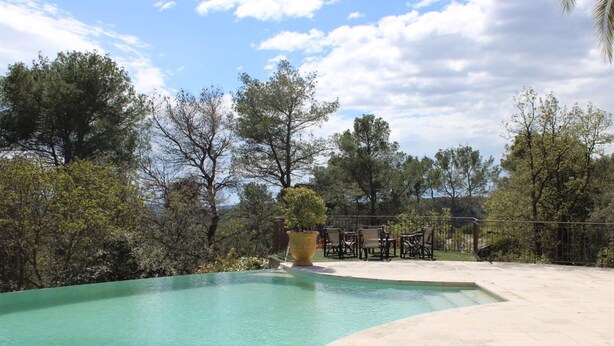 A swimming pool with a curved edge, surrounded by a patio area with outdoor furniture and a large planter. - Cueille la Nuit - TOURRETTES-SUR-LOUP (TOURRETTES-SUR-LOUP)