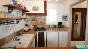 A compact kitchen with a sink, stove, microwave, and a small refrigerator. There are shelves with glassware and a clock on the wall. - Cueille la Nuit - TOURRETTES-SUR-LOUP (TOURRETTES-SUR-LOUP)