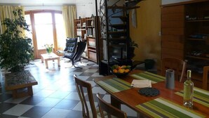 A cozy living room with a checkered floor, a wooden dining table, chairs, a sofa, a bookshelf, and a fireplace. - L'Oustaou - La Colle-sur-Loup (La Colle-sur-Loup)