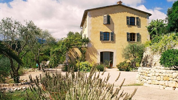 A two-story building with a stone facade, a central entrance, and a garden with various plants and a stone wall. - L'Oustaou - La Colle-sur-Loup (La Colle-sur-Loup)