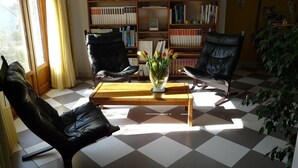 A room with a checkered floor, two leather chairs, a wooden coffee table with a vase of flowers, and bookshelves filled with books. - L'Oustaou - La Colle-sur-Loup (La Colle-sur-Loup)