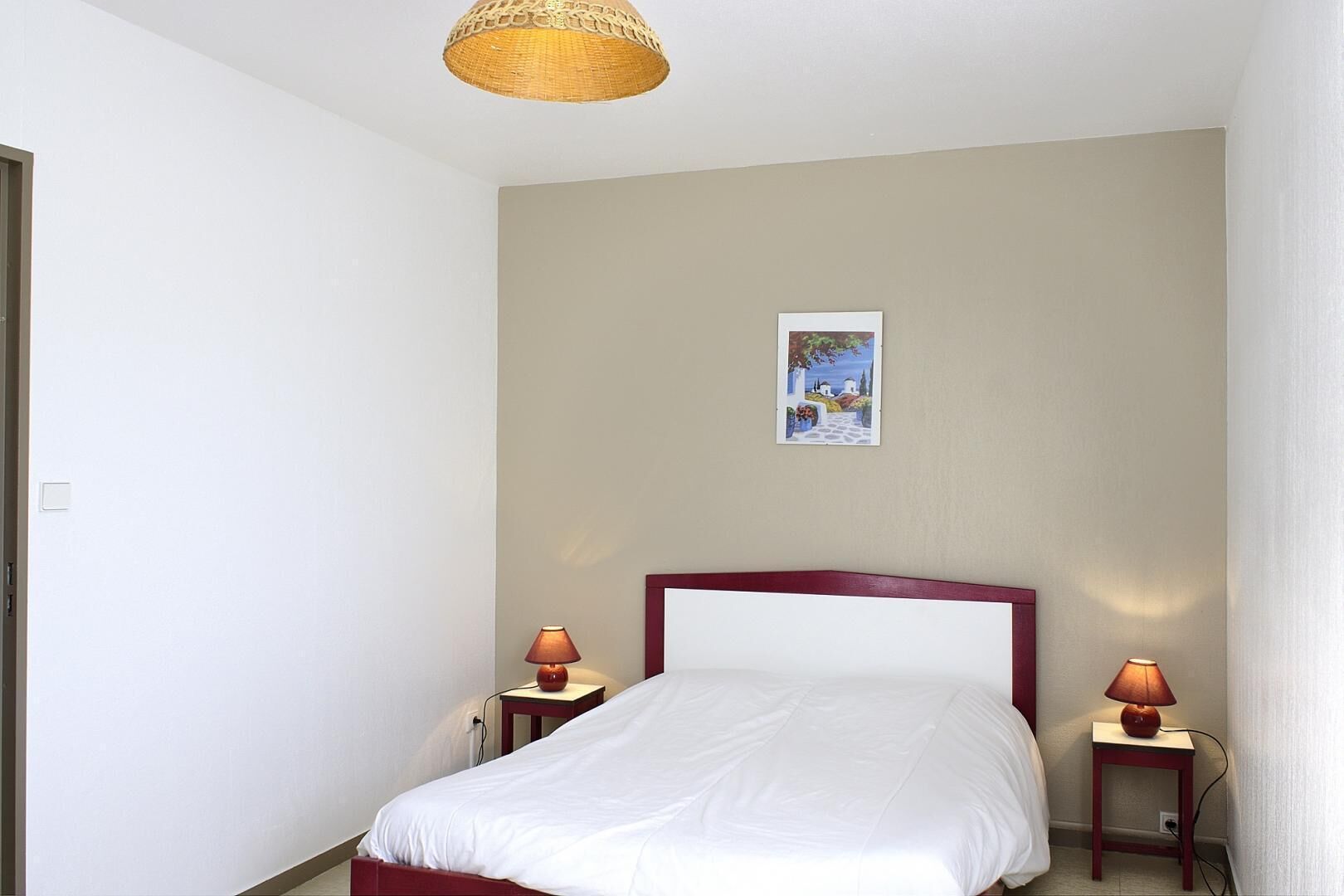 Un dormitorio con cama, dos mesitas de noche con lámparas, un cuadro en la pared y una lámpara del techo.