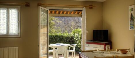 A room with a sliding door leading to a patio with a table and chairs, a radiator, a television, and a window with blinds.