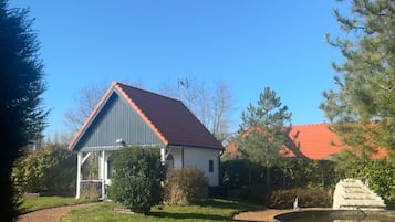 A house with a red roof and a grey exterior, surrounded by a well-maintained garden with a gravel path and a small pond.