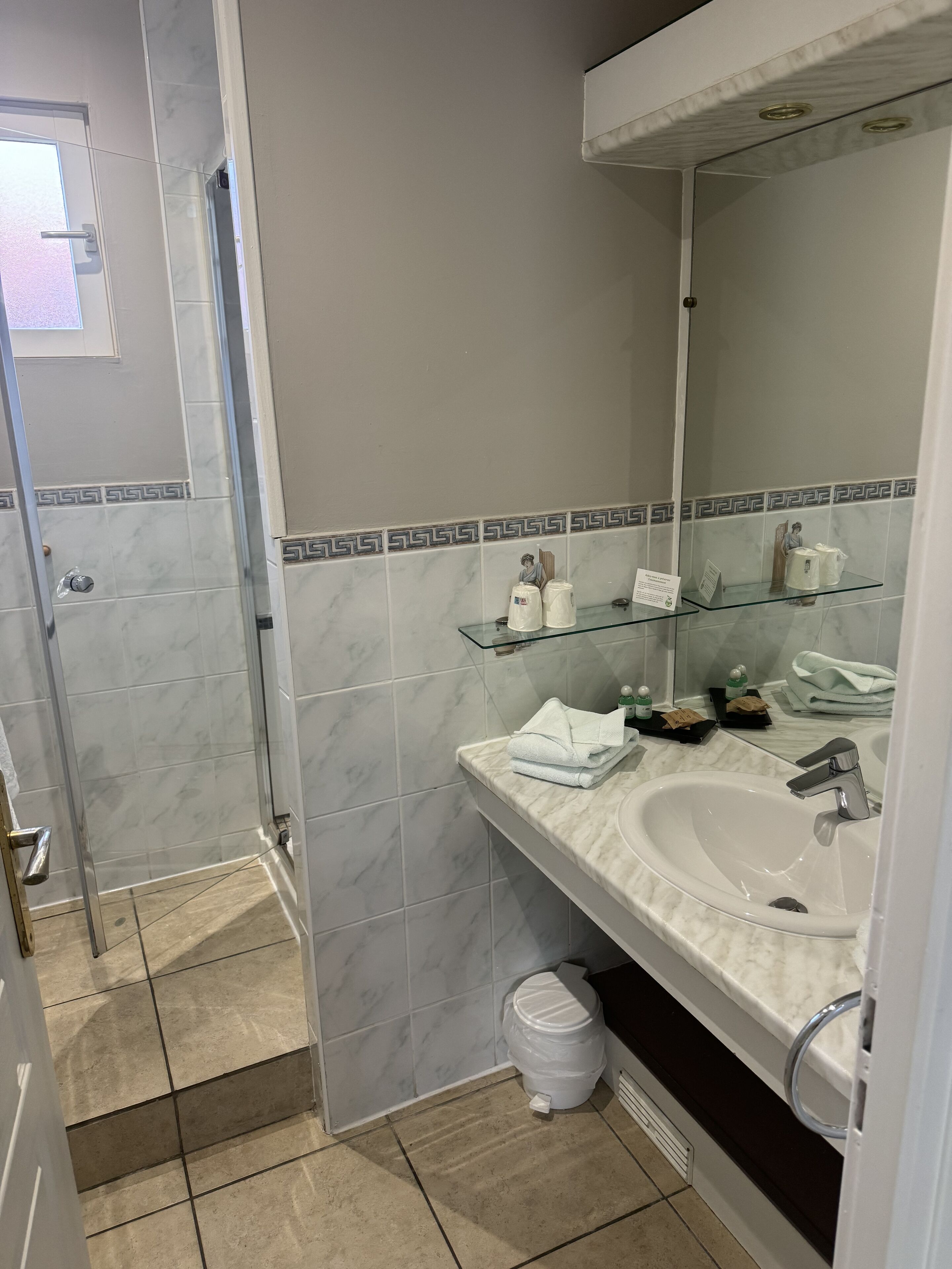 A bathroom with a marble-tiled wall, a glass shower enclosure, a sink with a mirror, and a toilet.