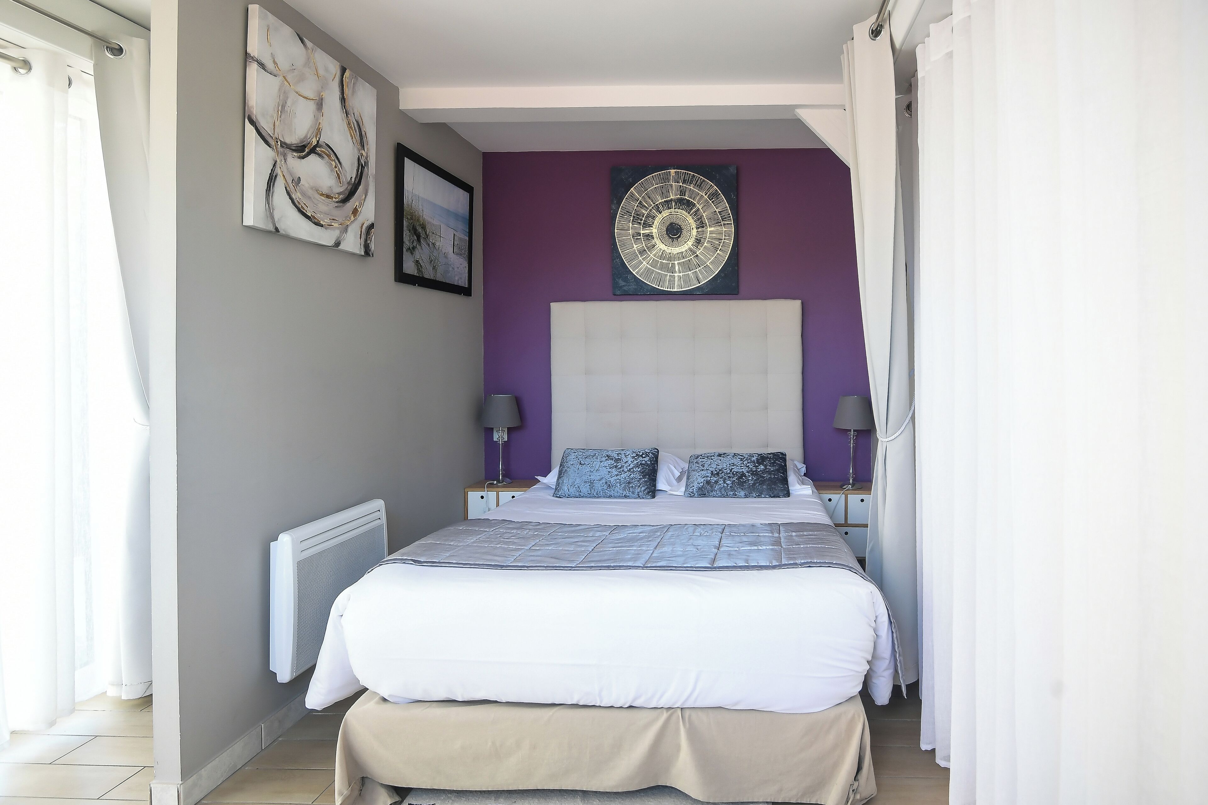 A bedroom with a large bed, a headboard, two bedside tables with lamps, and artwork on the walls.
