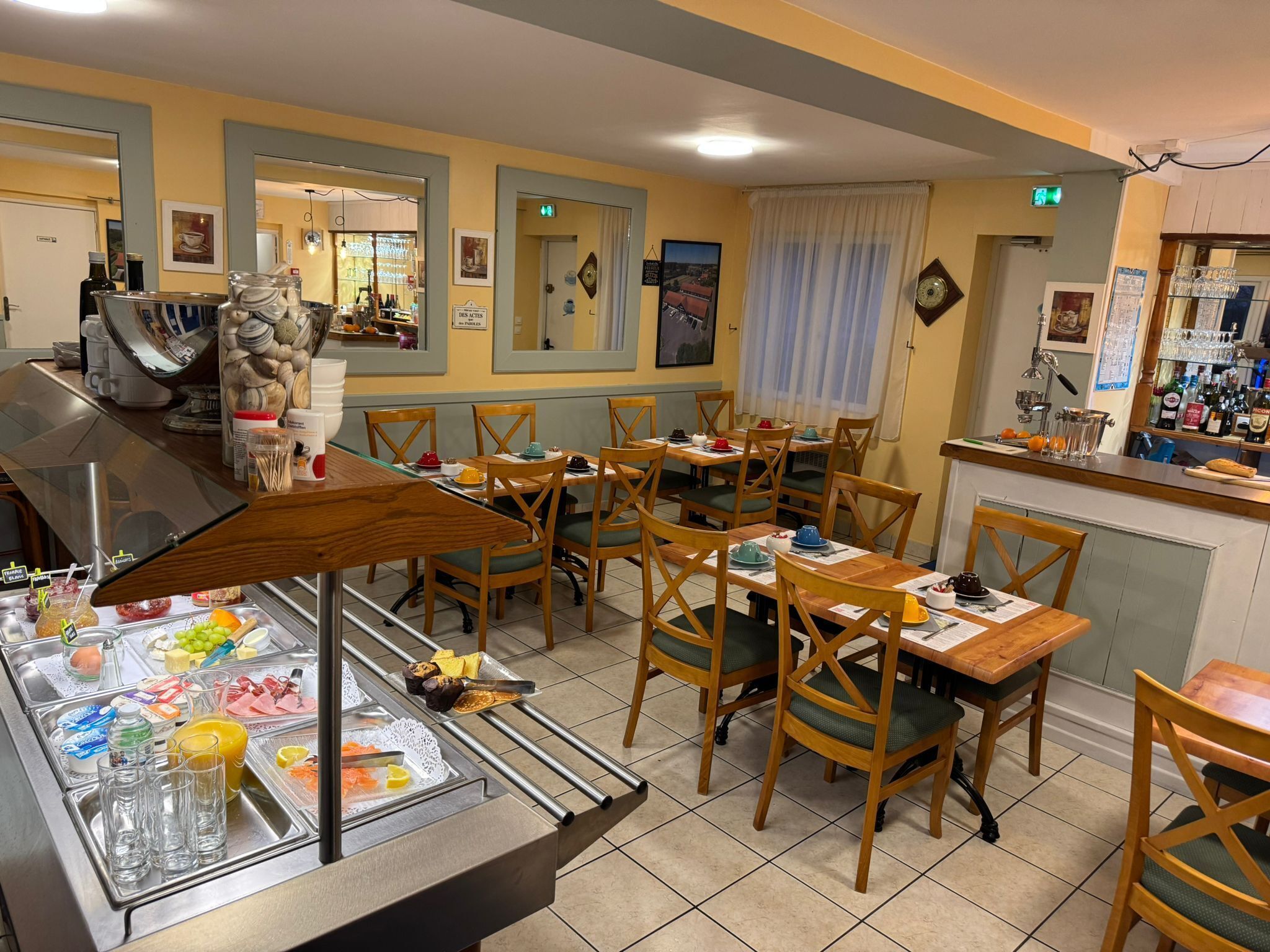 Un restaurante con varias mesas y sillas, una zona de bufé con diferentes alimentos y una barra con vasos y botellas.