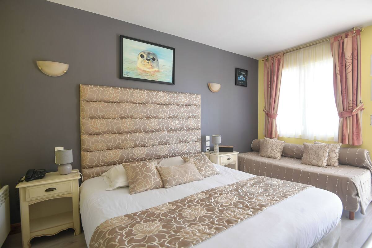 Une chambre d’hôtel avec un grand lit, un lit plus petit, une table de chevet avec une lampe et un tableau au mur.