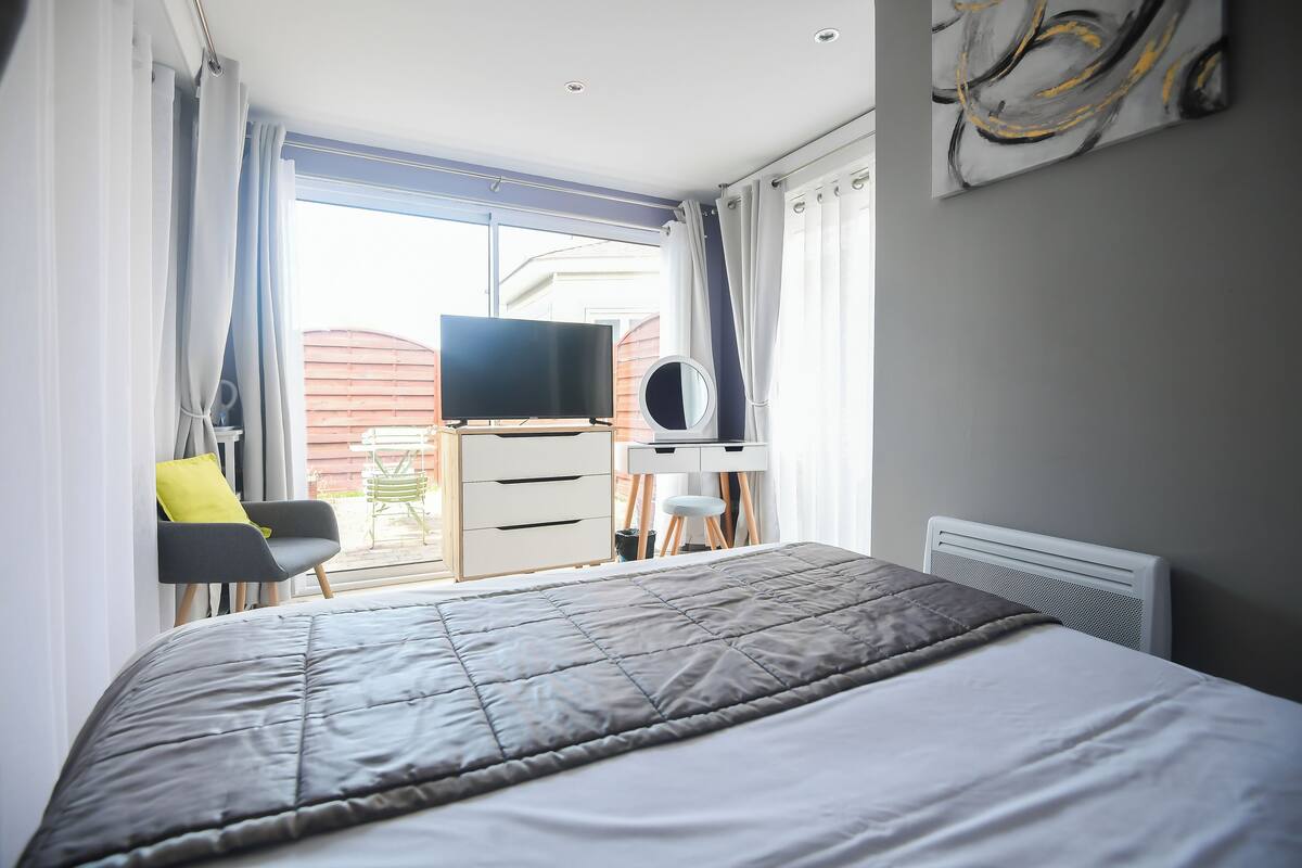 Une chambre à coucher avec un lit, un bureau, une chaise, un téléviseur et une fenêtre avec des rideaux.