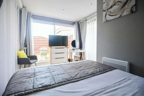 A bedroom with a bed, a desk, a chair, a television, and a window with curtains.