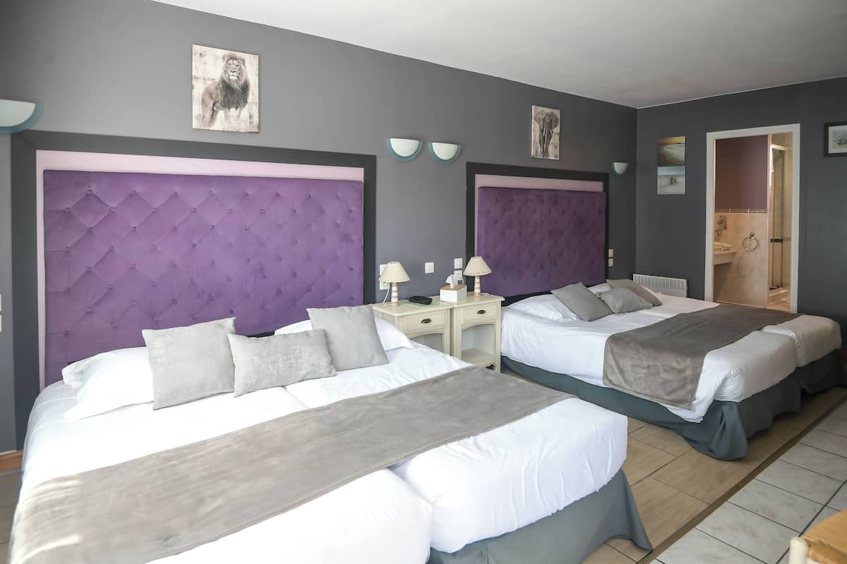 Une chambre d’hôtel avec deux lits, chacun doté d’une tête de lit violette, de draps blancs et d’un plaid gris. Il y a des tables de chevet avec des lampes et une petite table avec un téléphone.
