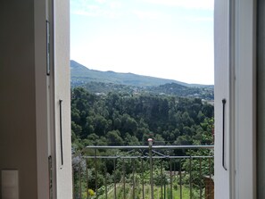 Une vue depuis un balcon dotĂ© dâune balustrade en mĂ©tal, donnant sur une zone densĂ©ment boisĂ©e avec des collines Ă lâhorizon.