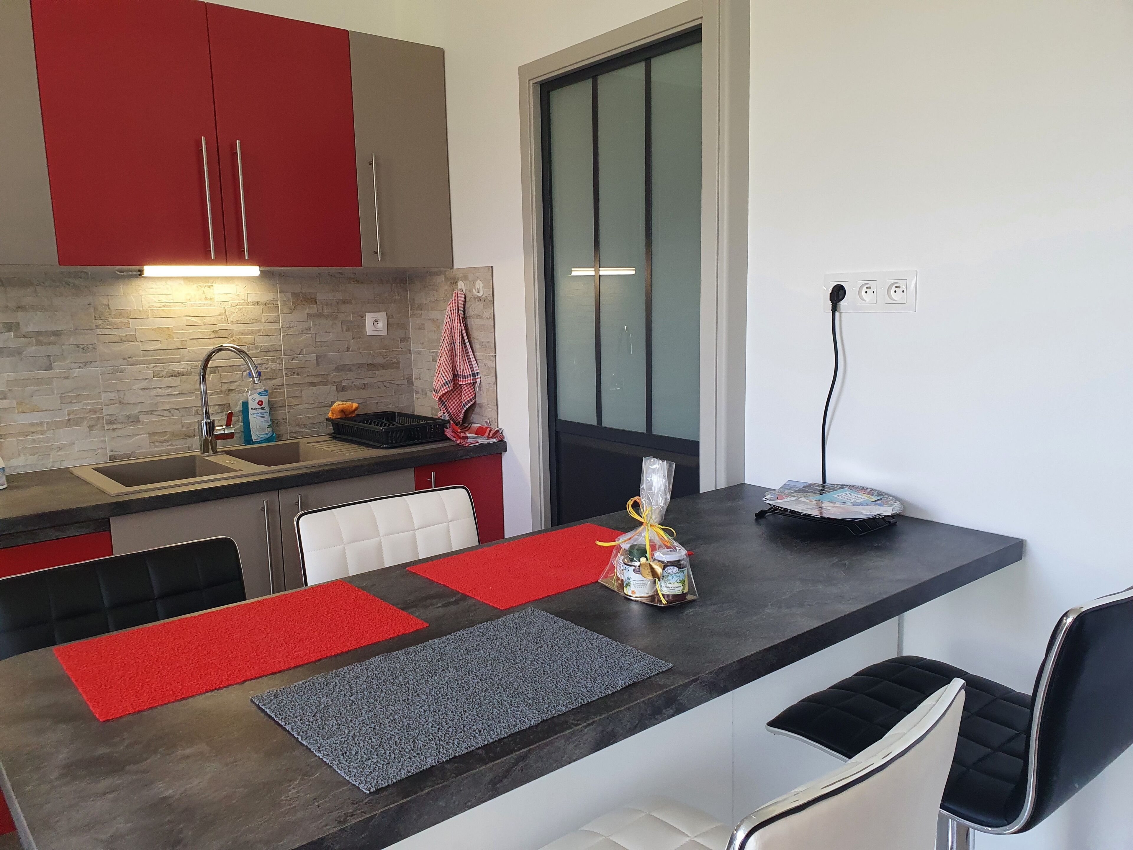 Uma cozinha moderna com armários vermelhos e cinzas, uma pia embutida e um espaço de jantar com bancada preta e tapetes vermelhos e cinzas.