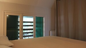 Un dormitorio con cama, ventana con persianas y cortina.
