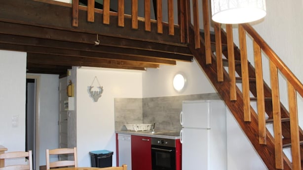 Una cocina con vigas de madera, una mesa de comedor, sillas, un refrigerador y un lavavajillas.