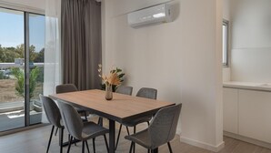 Ein zeitgemäßer Essbereich mit Holztisch und grauen Stühlen, einer Vase mit Trockenpflanzen und einem großen Fenster mit Blick auf Grünflächen und Gebäude.