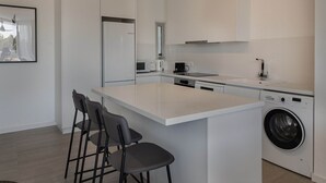 Een moderne keuken met een groot kookeiland, barkrukken, een ingebouwde wasmachine en een magnetron.