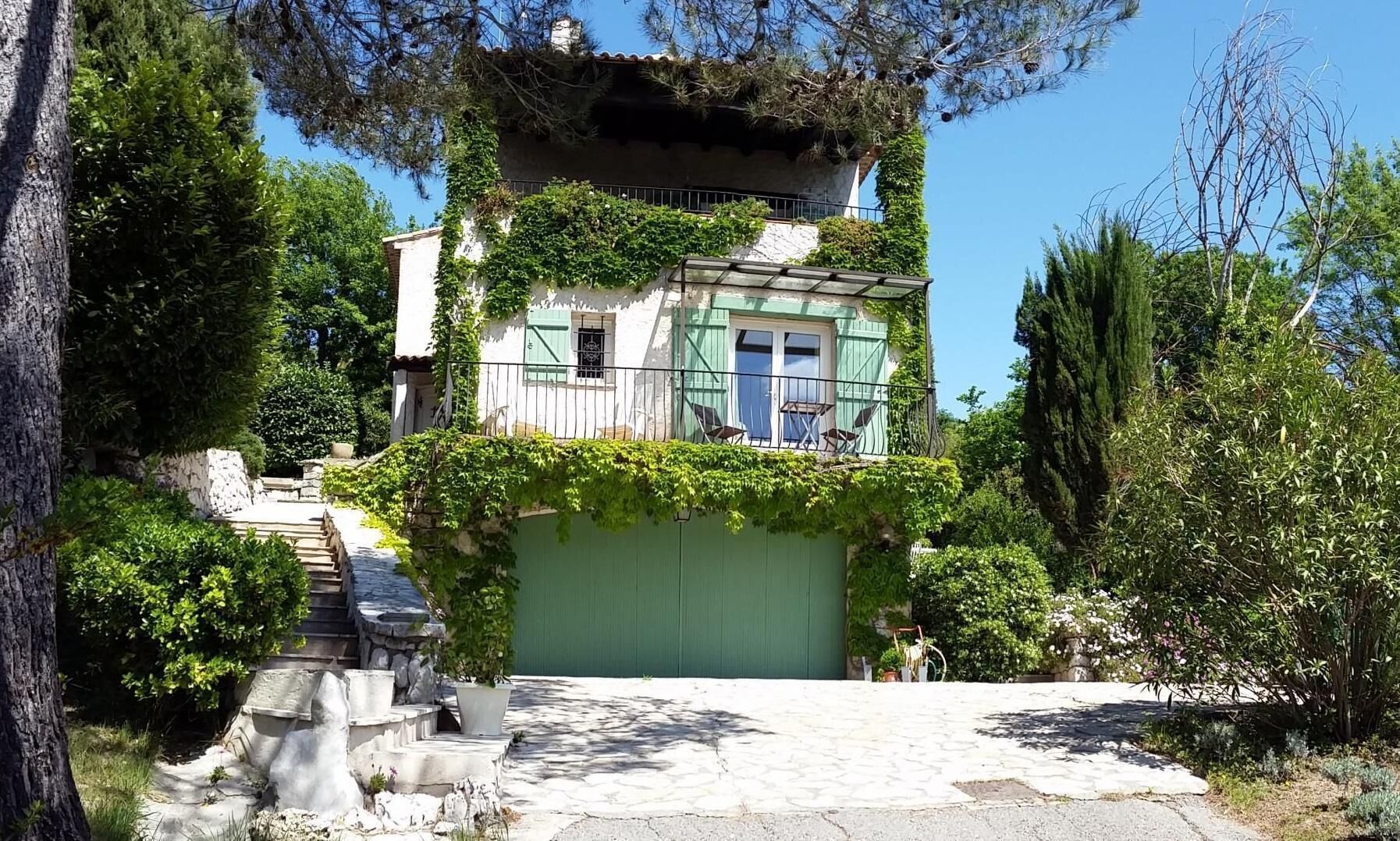 Um edifício de dois andares com uma porta verde e uma varanda com cadeiras.