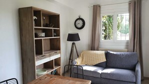 A living room with a wooden table, a grey sofa, a bookshelf, a lamp, and a window with curtains.