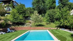 A rectangular swimming pool surrounded by a well-maintained lawn, with a brick wall and trees in the background.