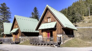 A row of wooden cabins with sloped roofs, a stone wall, and a gravel path leading to them.
