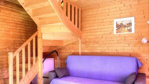 A wooden cabin interior with a wooden staircase, a purple sofa, and a small table with a lamp.