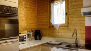 A compact kitchen with wooden walls, a built-in oven, a coffee maker, and a sink.