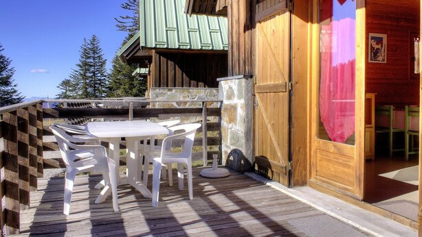 A wooden cabin with a wooden deck, a table with chairs, and a door with a curtain.