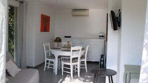 A compact kitchen with white cabinetry, a dining table with chairs, a small side table, and a TV mounted on the wall.