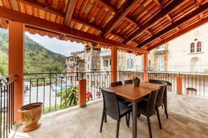 Un balcon avec une table et des chaises en bois, un pot de fleurs et une vue sur une rue animée, avec des voitures et des immeubles.